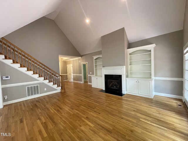 21 Covington Ln, Durham, NC 27712 - unfurnished living room with stairway, built in features, high vaulted ceiling, wood finished floors, and a fireplace with flush hearth