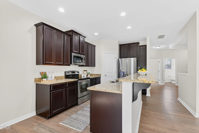 4520 Middletown Dr, Wake Forest, NC 27587 - kitchen with stainless steel appliances, dark brown cabinetry, light wood finished floors, a kitchen bar, and light stone countertops