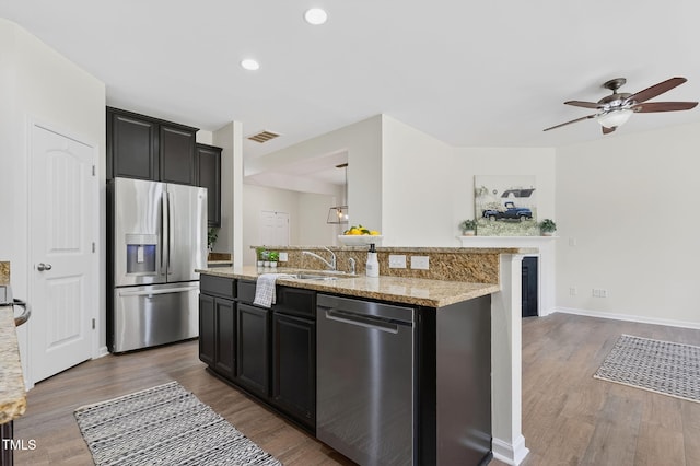 4520 Middletown Dr, Wake Forest, NC 27587 - kitchen featuring appliances with stainless steel finishes, ceiling fan, wood finished floors, a kitchen island with sink, and light stone counters