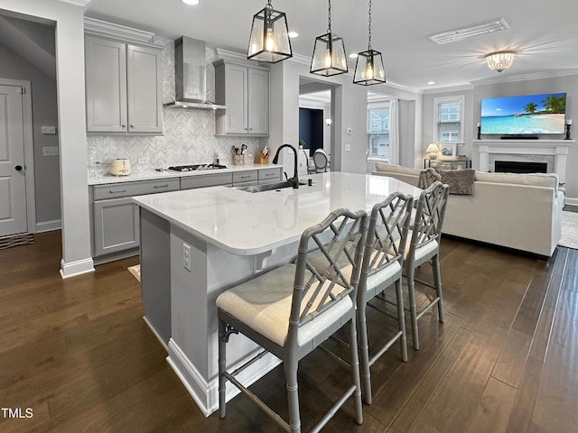 2438 Braxton Wood Ln, Apex, NC 27523 - kitchen with gray cabinetry, wall chimney range hood, gas stovetop, ornamental molding, and a breakfast bar area