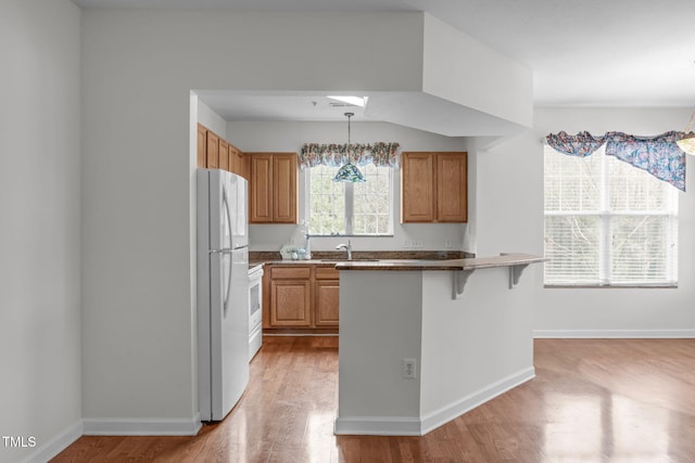 232 Eyam Hall Ln, Apex, NC 27502 - kitchen featuring freestanding refrigerator, light wood-style flooring, a kitchen bar, pendant lighting, and brown cabinetry