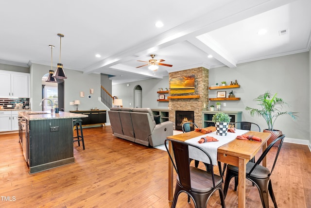 3313 Bentwinds Bluffs Ln, Fuquay Varina, NC 27526 - dining room featuring a ceiling fan, beam ceiling, a stone fireplace, light wood-style flooring, and ornamental molding
