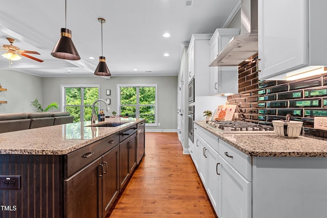 3313 Bentwinds Bluffs Ln, Fuquay Varina, NC 27526 - kitchen featuring wall chimney exhaust hood, dark brown cabinets, white cabinetry, appliances with stainless steel finishes, and light wood finished floors