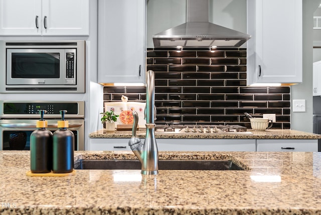 3313 Bentwinds Bluffs Ln, Fuquay Varina, NC 27526 - kitchen with wall chimney exhaust hood, appliances with stainless steel finishes, white cabinetry, and light stone counters