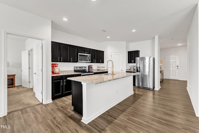 133 Ogden Pond Pl, Zebulon, NC 27597 - kitchen with stainless steel appliances, dark cabinetry, light wood-type flooring, light stone countertops, and recessed lighting