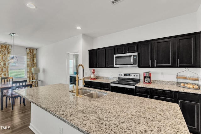 133 Ogden Pond Pl, Zebulon, NC 27597 - kitchen featuring appliances with stainless steel finishes, dark cabinets, recessed lighting, light stone counters, and a kitchen island with sink
