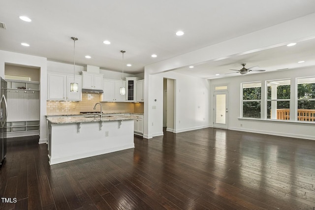 261 Begen St, Morrisville, NC 27560 - kitchen featuring a ceiling fan, under cabinet range hood, a kitchen island with sink, decorative backsplash, and a kitchen bar