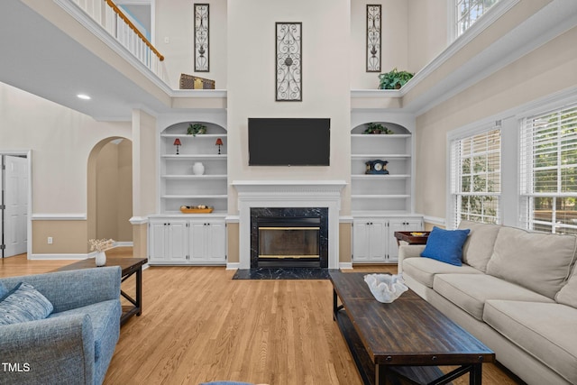 3608 Smoky Chestnut Ln, Raleigh, NC 27615 - living room with built in features, a towering ceiling, light wood finished floors, a high end fireplace, and arched walkways