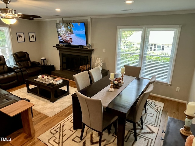 1507 Woodcroft Dr, Raleigh, NC 27609 - dining space featuring crown molding, light wood-style flooring, plenty of natural light, a fireplace with raised hearth, and a ceiling fan