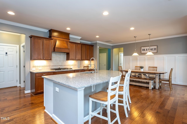 3913 Chapel Oak Dr, Apex, NC 27502 - kitchen featuring brown cabinetry, dark wood-type flooring, light stone counters, backsplash, and a kitchen island with sink