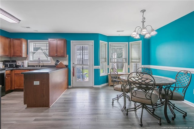 1214 Herring Gull Dr, Fayetteville, NC 28306 - kitchen with dark countertops, a chandelier, a peninsula, brown cabinets, and wood finished floors