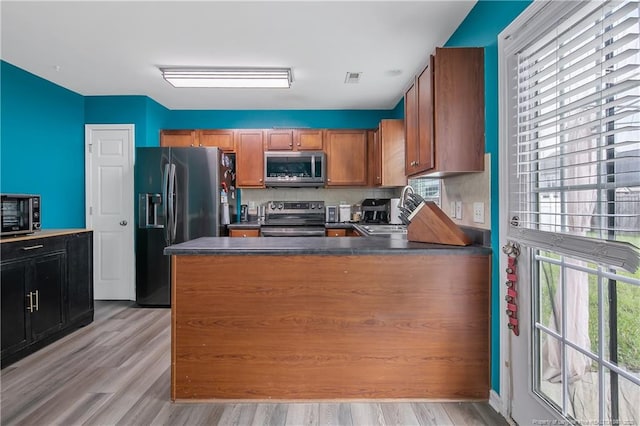1214 Herring Gull Dr, Fayetteville, NC 28306 - kitchen featuring stainless steel appliances, dark countertops, brown cabinets, light wood finished floors, and a peninsula