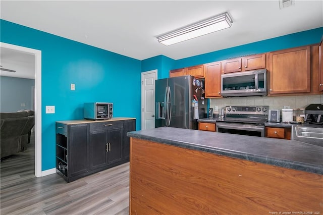 1214 Herring Gull Dr, Fayetteville, NC 28306 - kitchen featuring appliances with stainless steel finishes, dark countertops, light wood finished floors, tasteful backsplash, and a peninsula