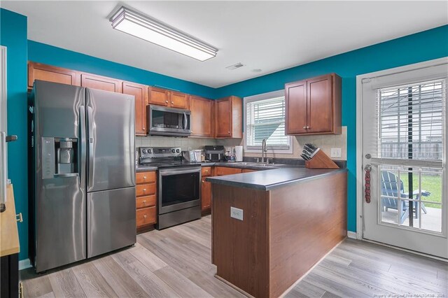 1214 Herring Gull Dr, Fayetteville, NC 28306 - kitchen with stainless steel appliances, dark countertops, a peninsula, light wood finished floors, and backsplash