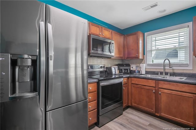 1214 Herring Gull Dr, Fayetteville, NC 28306 - kitchen with appliances with stainless steel finishes, dark countertops, light wood finished floors, brown cabinets, and backsplash