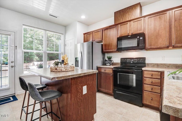 100 Stratford Lakes Dr # 322, Durham, NC 27713 - kitchen featuring black appliances, a center island, a breakfast bar area, light countertops, and brown cabinetry