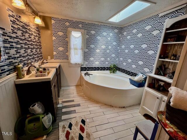 174 Daffodil Dr, Henderson, NC 27537 - bathroom featuring vanity, a textured ceiling, a garden tub, a skylight, and a wainscoted wall