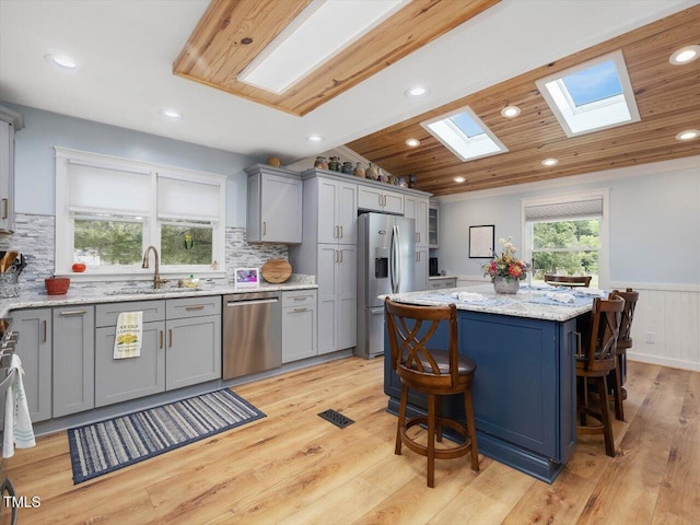 358 Benjie Williams Rd, Staley, NC 27355 - kitchen featuring appliances with stainless steel finishes, a skylight, gray cabinetry, wainscoting, and a kitchen bar