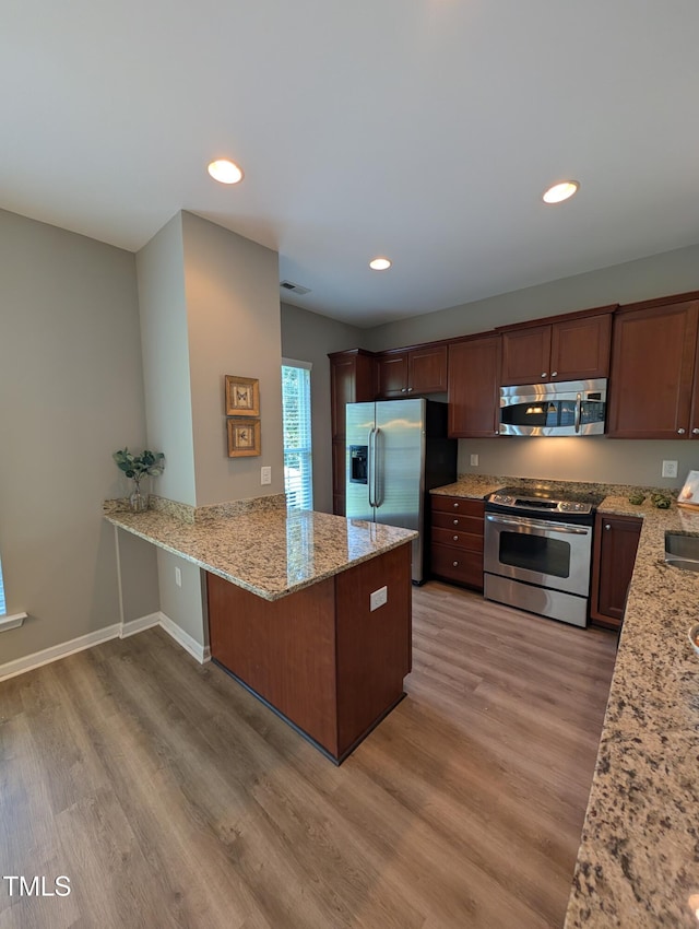 4221 Del Webb Ave, Cary, NC 27519 - kitchen featuring appliances with stainless steel finishes, a peninsula, light wood-style floors, light stone counters, and recessed lighting