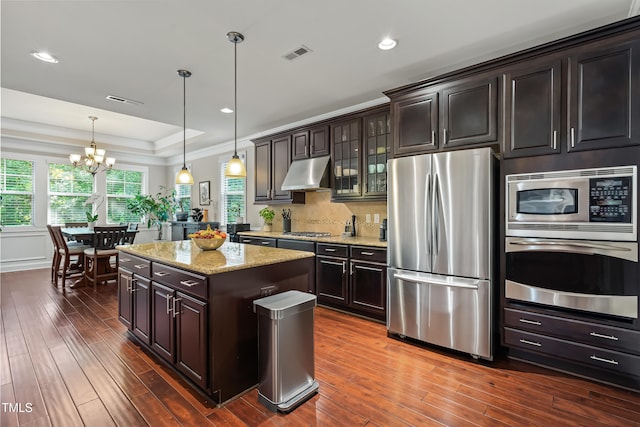 5116 Trembath Ln, Cary, NC 27519 - kitchen with stainless steel appliances, under cabinet range hood, a chandelier, dark wood-type flooring, and light stone countertops