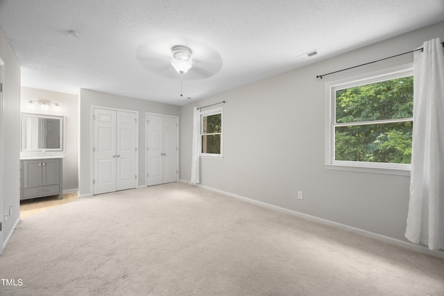 122 Woodbridge Ln, Chapel Hill, NC 27514 - unfurnished bedroom with multiple closets, light colored carpet, a textured ceiling, a ceiling fan, and ensuite bath