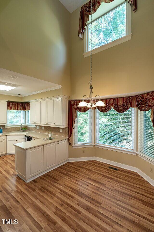 103 Glenstone Ln, Cary, NC 27518 - kitchen with white cabinets, light wood-type flooring, light countertops, a chandelier, and a peninsula