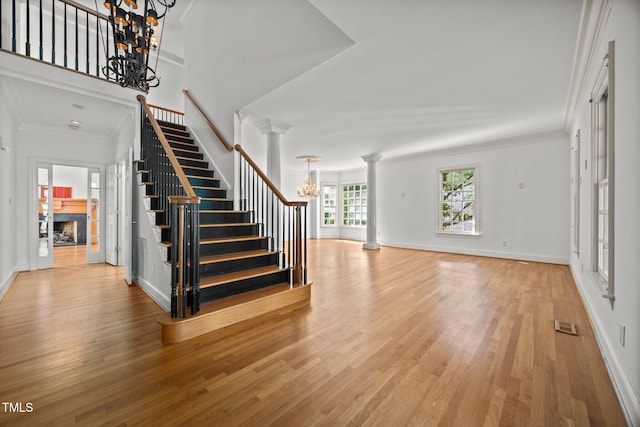 3604 Eden Croft Dr, Raleigh, NC 27612 - unfurnished living room with a chandelier, ornate columns, stairway, light wood-style floors, and a fireplace