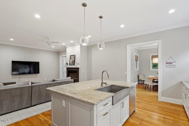 1103 Roosevelt Dr, Chapel Hill, NC 27514 - kitchen with stainless steel dishwasher, light wood finished floors, an island with sink, ornamental molding, and white cabinetry