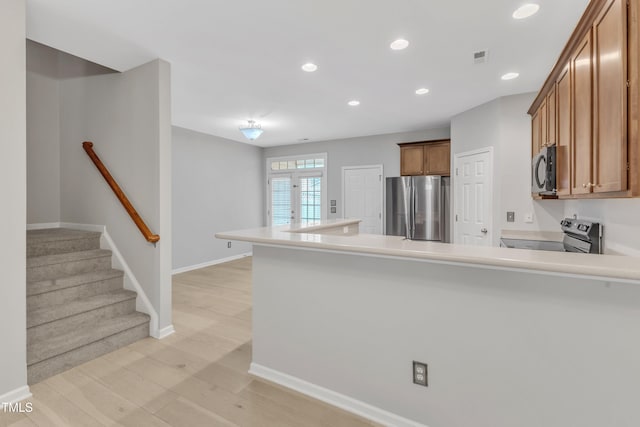 3634 Olympia Dr, Raleigh, NC 27603 - kitchen featuring appliances with stainless steel finishes, a peninsula, brown cabinetry, light countertops, and light wood finished floors