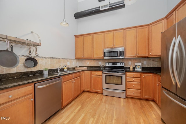 1535 Caraleigh Mills Ct Unit 142, Raleigh, NC 27603 - kitchen featuring stainless steel appliances, backsplash, light wood-style floors, a towering ceiling, and dark stone countertops