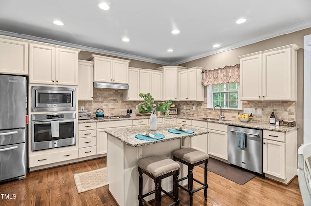 2712 Lake Waccamaw Trl, Apex, NC 27502 - kitchen featuring appliances with stainless steel finishes, under cabinet range hood, crown molding, a breakfast bar area, and decorative backsplash