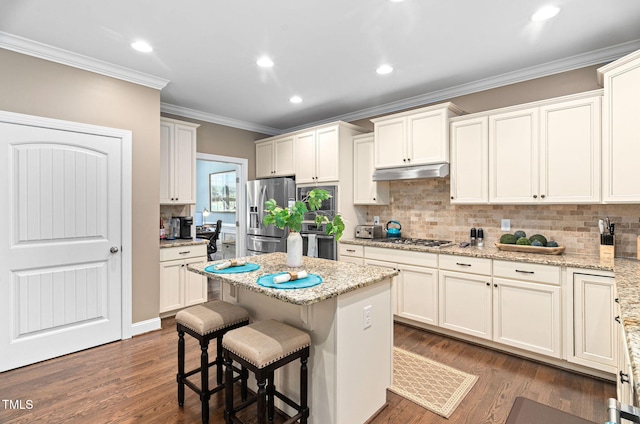 2712 Lake Waccamaw Trl, Apex, NC 27502 - kitchen with appliances with stainless steel finishes, under cabinet range hood, a kitchen breakfast bar, backsplash, and crown molding