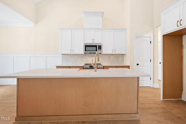 140 Purslane Dr, Franklinton, NC 27525 - kitchen featuring stainless steel microwave, backsplash, an island with sink, light wood-style flooring, and light countertops