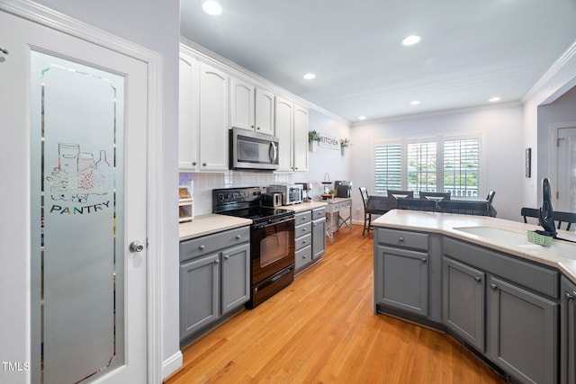 1824 Ferrell Meadows Dr, Zebulon, NC 27597 - kitchen with black range with electric cooktop, stainless steel microwave, gray cabinets, white cabinetry, and light wood finished floors