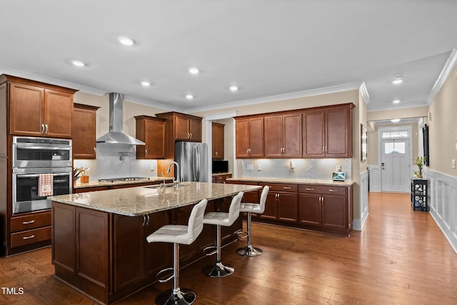 8713 Halsey Ln, Wake Forest, NC 27587 - kitchen featuring wall chimney exhaust hood, appliances with stainless steel finishes, ornamental molding, light stone countertops, and a center island with sink