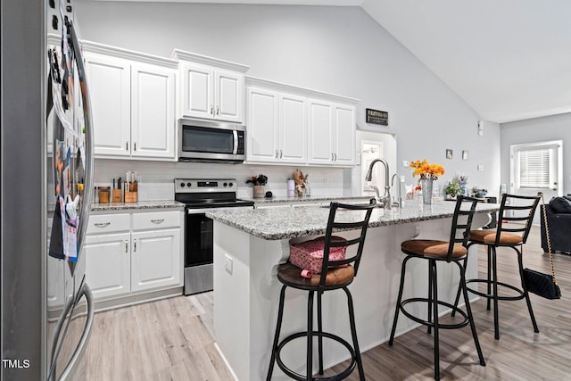 9448 S Beaver Creek Way, Middlesex, NC 27557 - kitchen with stainless steel appliances, high vaulted ceiling, a kitchen breakfast bar, white cabinets, and light wood-type flooring