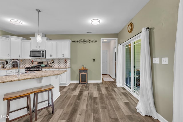 450 Cotton Mill Dr, Zebulon, NC 27597 - kitchen with appliances with stainless steel finishes, a breakfast bar, white cabinets, tasteful backsplash, and wood finished floors