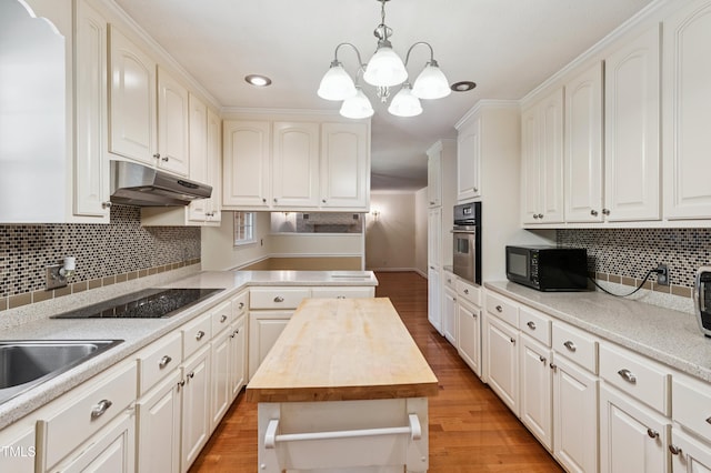 410 Sherron Rd, Durham, NC 27703 - kitchen featuring under cabinet range hood, black appliances, tasteful backsplash, hanging light fixtures, and light wood-type flooring