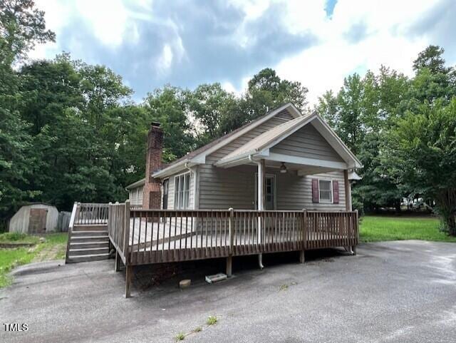 2856 Nutbush Rd, Henderson, NC 27537 - view of front facade featuring a storage unit, a deck, a chimney, and view of scattered trees
