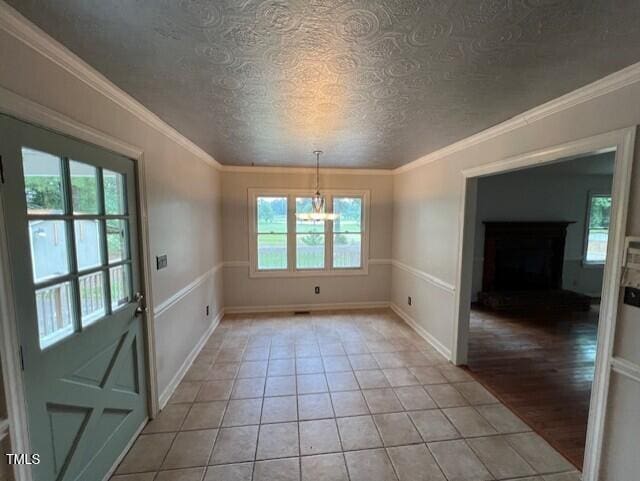 2856 Nutbush Rd, Henderson, NC 27537 - unfurnished dining area with plenty of natural light, a chandelier, a textured ceiling, a fireplace with raised hearth, and ornamental molding