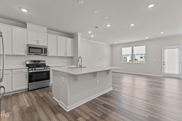 5721 Woodlawn Dr, Durham, NC 27703 - kitchen featuring appliances with stainless steel finishes, ornamental molding, light countertops, an island with sink, and wood finished floors