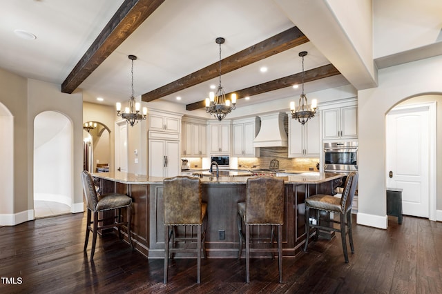 19 San Rimini Way, Durham, NC 27707 - kitchen featuring custom range hood, arched walkways, decorative backsplash, a large island with sink, and beamed ceiling