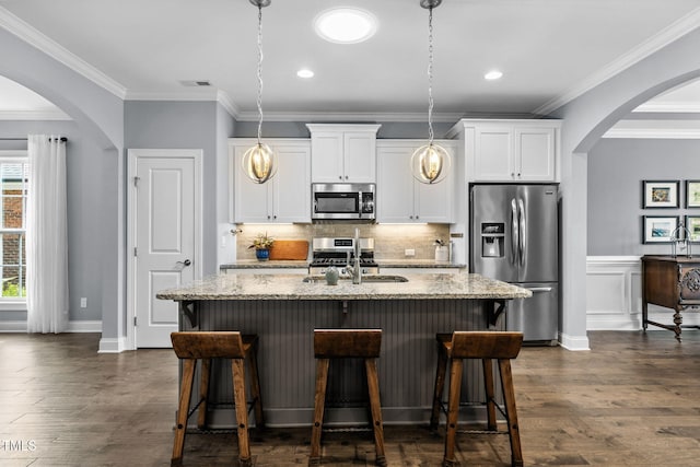 124 Moss Creek Pl, Fuquay Varina, NC 27526 - kitchen featuring appliances with stainless steel finishes, white cabinetry, arched walkways, light stone countertops, and crown molding