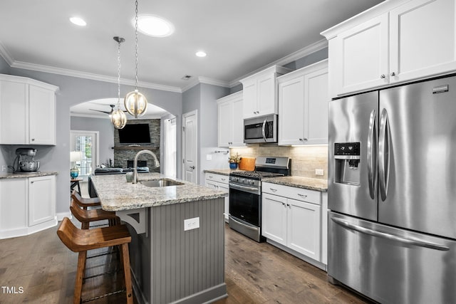 124 Moss Creek Pl, Fuquay Varina, NC 27526 - kitchen featuring appliances with stainless steel finishes, arched walkways, crown molding, white cabinetry, and a center island with sink
