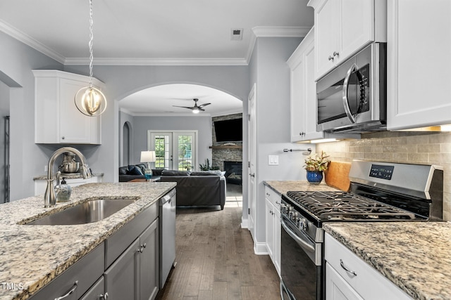 124 Moss Creek Pl, Fuquay Varina, NC 27526 - kitchen featuring stainless steel appliances, arched walkways, ceiling fan, a stone fireplace, and dark wood-style floors