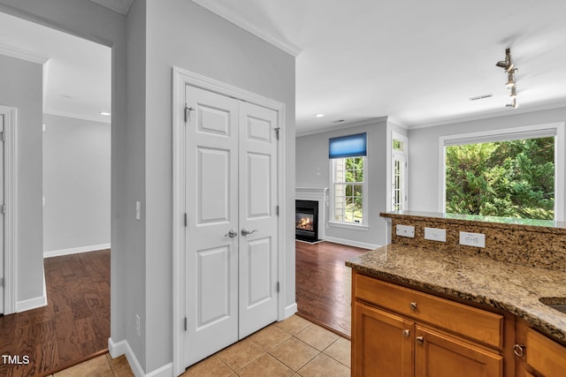5515 S Roxboro St Unit 3, Durham, NC 27713 - kitchen with ornamental molding, stone countertops, brown cabinets, a glass covered fireplace, and light tile patterned floors