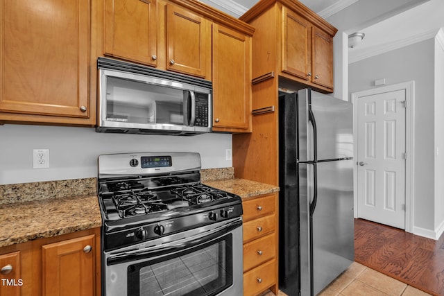 5515 S Roxboro St Unit 3, Durham, NC 27713 - kitchen featuring appliances with stainless steel finishes, ornamental molding, brown cabinets, light stone counters, and light tile patterned floors