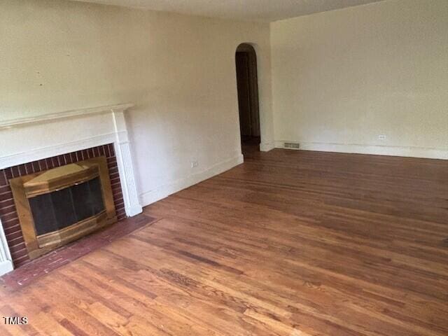 1414 Vickers Ave, Durham, NC 27707 - unfurnished living room featuring arched walkways, wood finished floors, and a brick fireplace