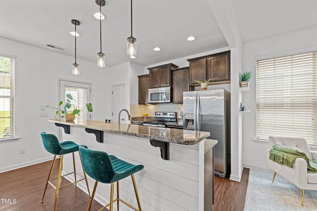 2700 Benevolence Dr, Raleigh, NC 27610 - kitchen with appliances with stainless steel finishes, a kitchen breakfast bar, dark brown cabinets, tasteful backsplash, and dark wood-style flooring