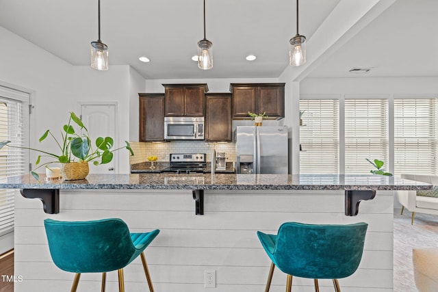 2700 Benevolence Dr, Raleigh, NC 27610 - kitchen with appliances with stainless steel finishes, dark brown cabinets, decorative backsplash, dark stone counters, and a kitchen breakfast bar